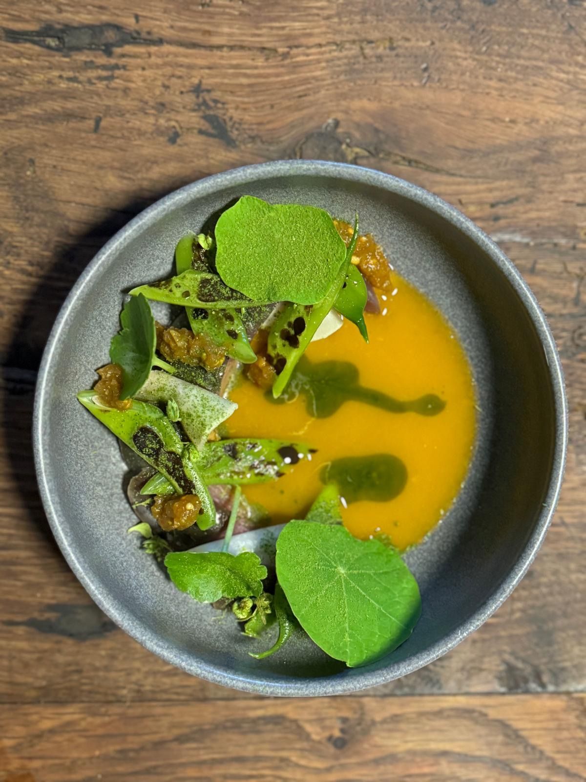 a grey bowl with orange broth, beans and nasturtium leaves