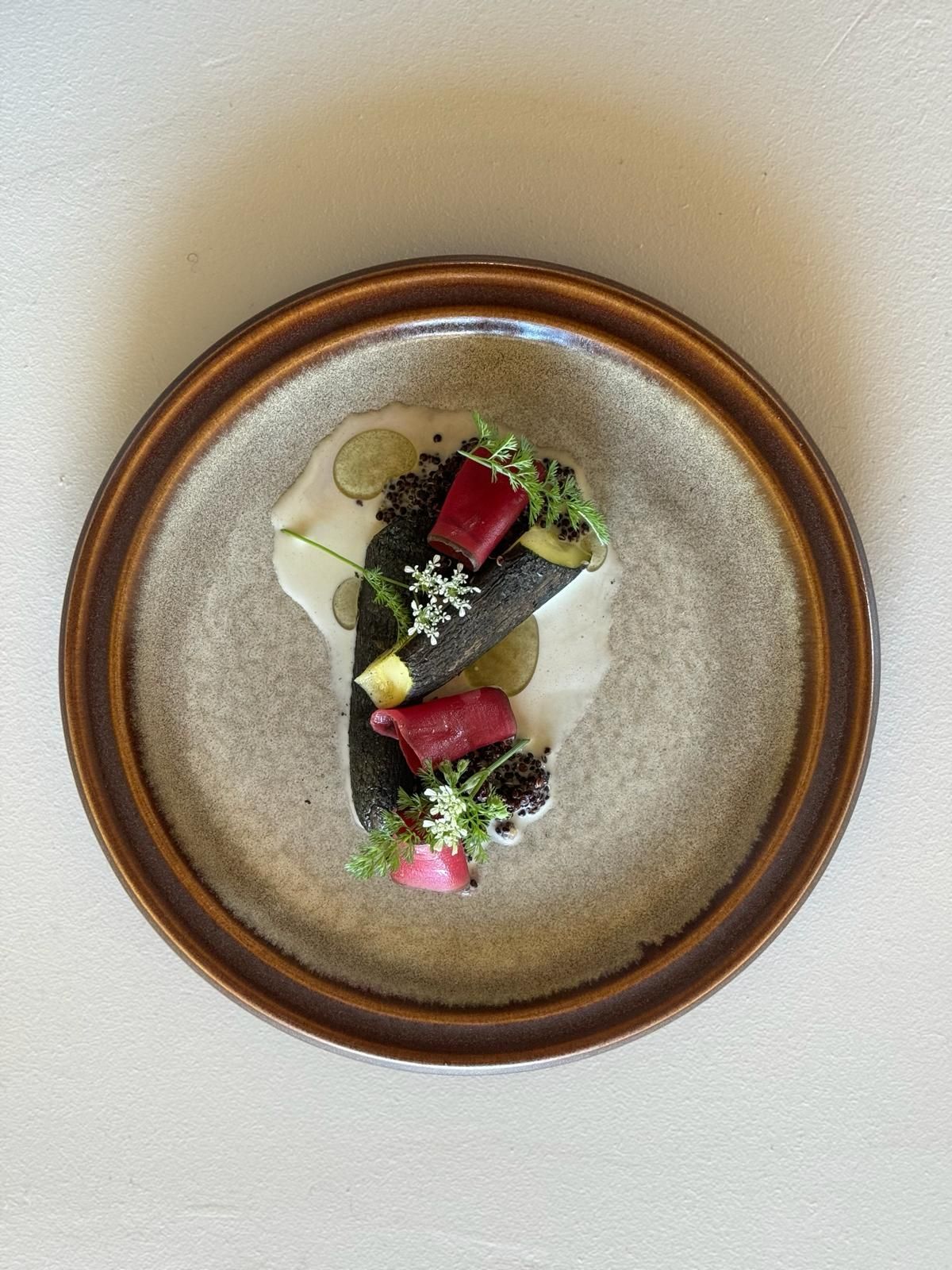 charred root with beetroot and wild carrot flowers on a stoneware plate